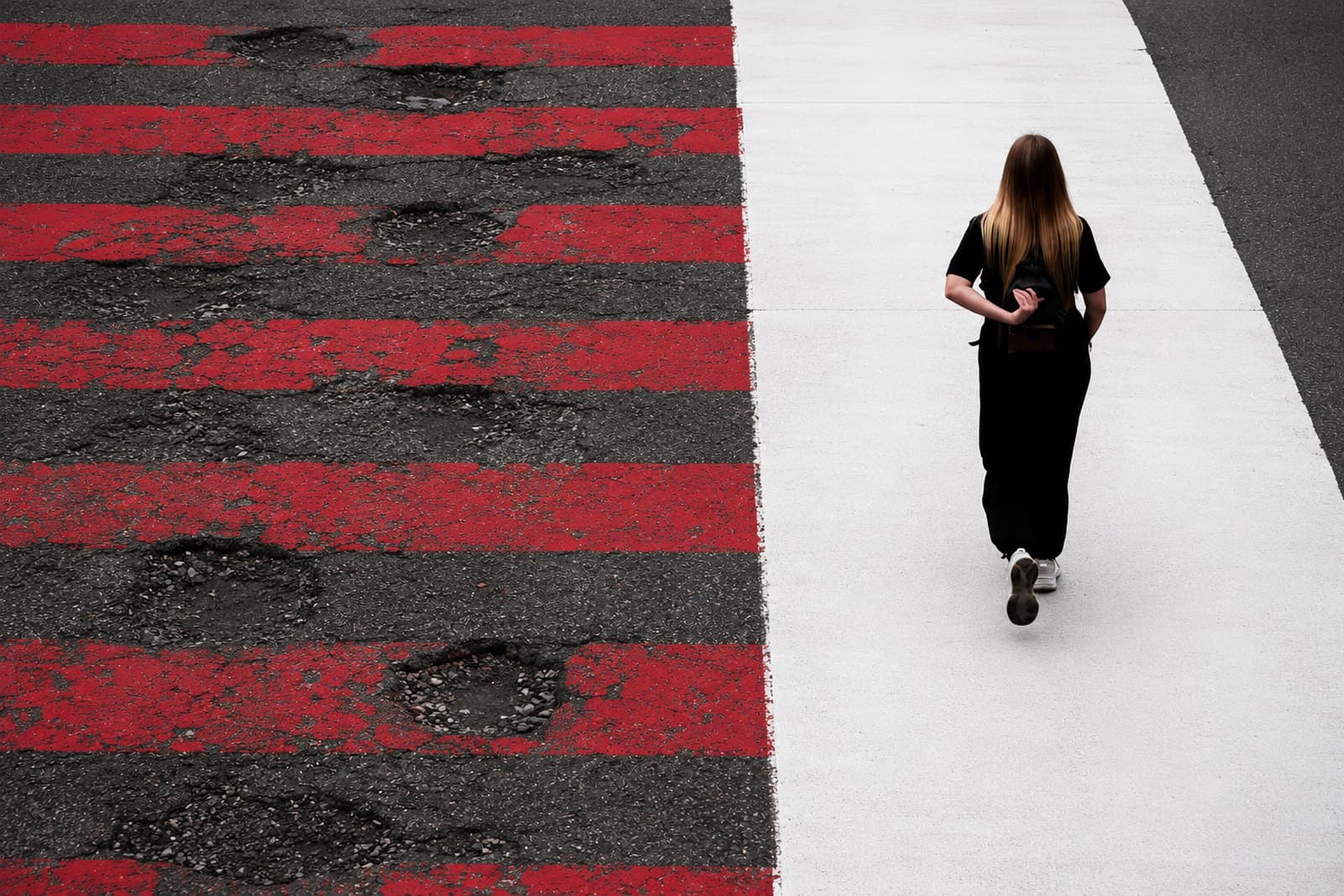 A person walking a clear white path beside a cracked, patched road, a route without the usual obstacles.